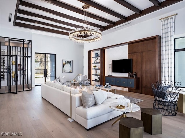 living room featuring an inviting chandelier, beam ceiling, light hardwood / wood-style flooring, and french doors