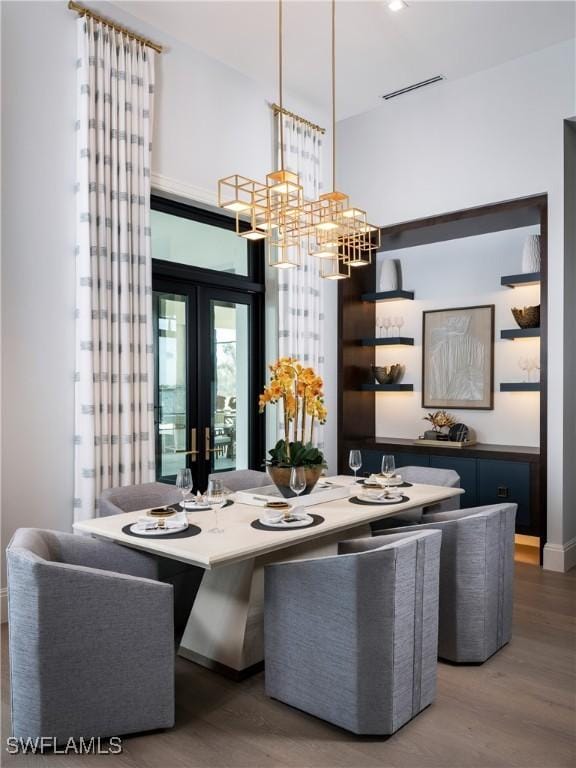 dining area with wood-type flooring, a notable chandelier, and french doors