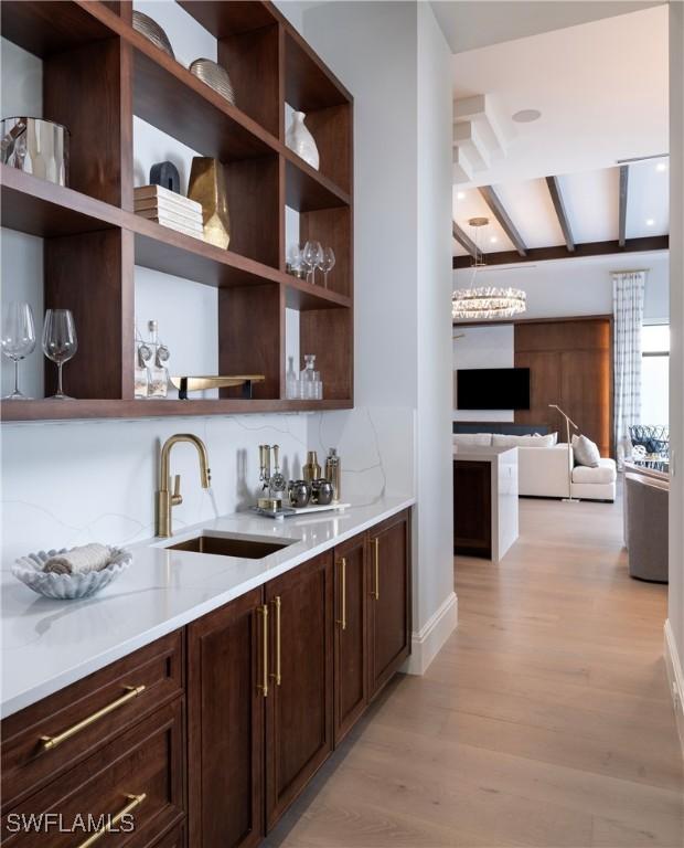 bar featuring dark brown cabinetry, sink, decorative backsplash, and light wood-type flooring