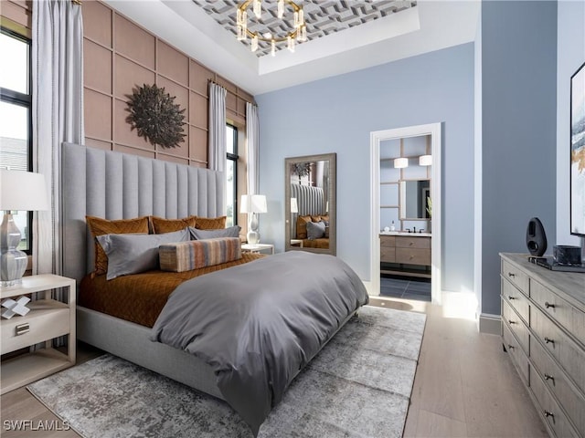 bedroom with ensuite bath, a raised ceiling, a notable chandelier, and light wood-type flooring