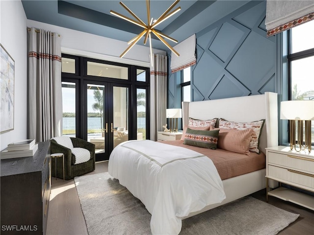 bedroom with multiple windows, a water view, hardwood / wood-style floors, and french doors