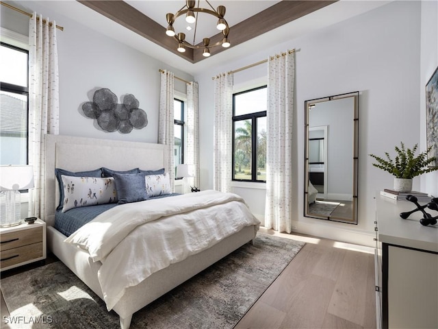 bedroom with hardwood / wood-style flooring, a notable chandelier, and a tray ceiling