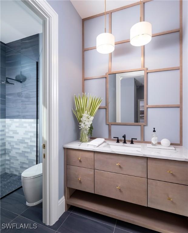 bathroom featuring a tile shower, vanity, tile patterned flooring, and toilet