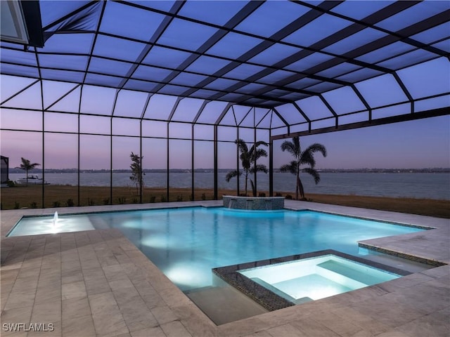 pool at dusk featuring an in ground hot tub, pool water feature, glass enclosure, a water view, and a patio area