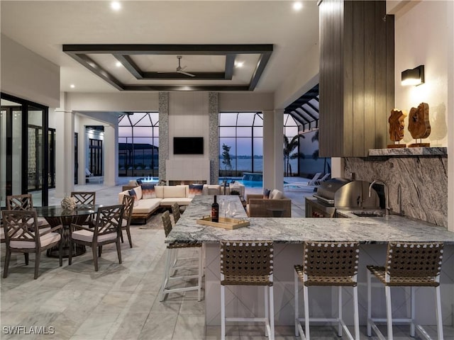 kitchen featuring light stone countertops, a raised ceiling, kitchen peninsula, and a kitchen bar