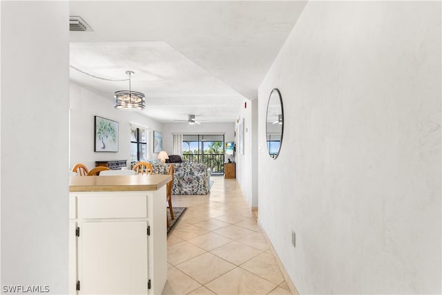 kitchen with kitchen peninsula, ceiling fan with notable chandelier, light tile patterned floors, decorative light fixtures, and white cabinetry