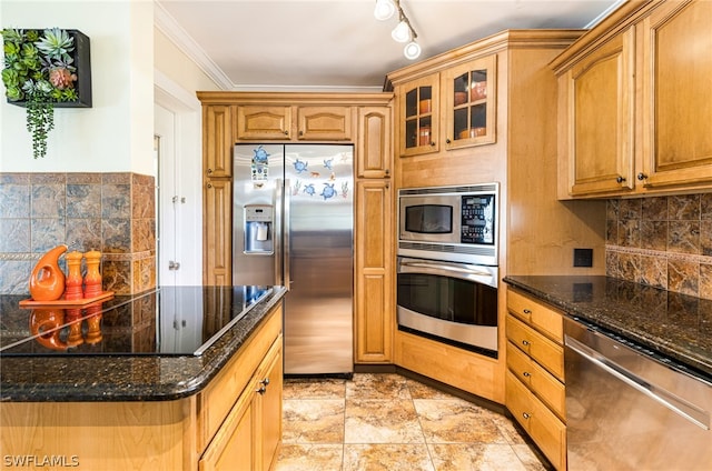 kitchen featuring backsplash, dark stone counters, track lighting, crown molding, and appliances with stainless steel finishes