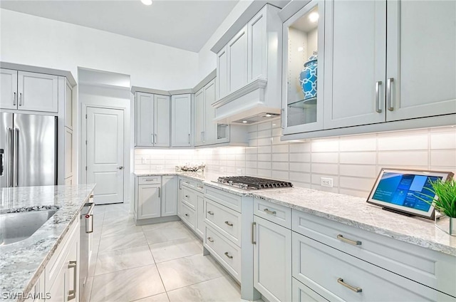 kitchen featuring backsplash, light stone countertops, stainless steel appliances, and premium range hood