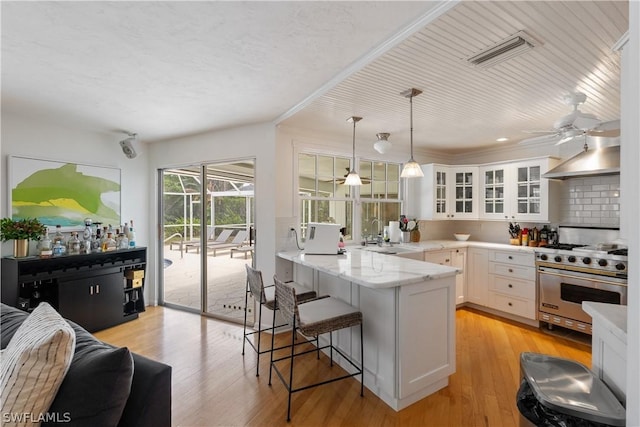 kitchen featuring a breakfast bar, luxury range, white cabinetry, hanging light fixtures, and kitchen peninsula