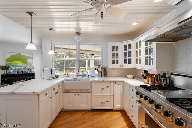 kitchen with white cabinets, luxury range, hanging light fixtures, and wall chimney range hood