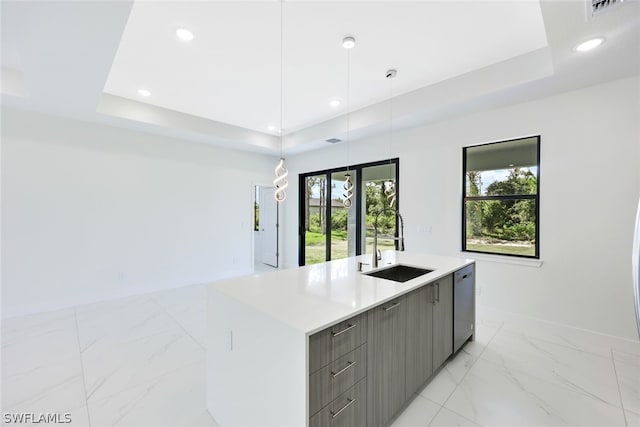 kitchen featuring sink, a raised ceiling, stainless steel dishwasher, decorative light fixtures, and a kitchen island with sink