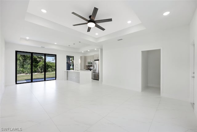 unfurnished living room featuring a raised ceiling, ceiling fan, and sink