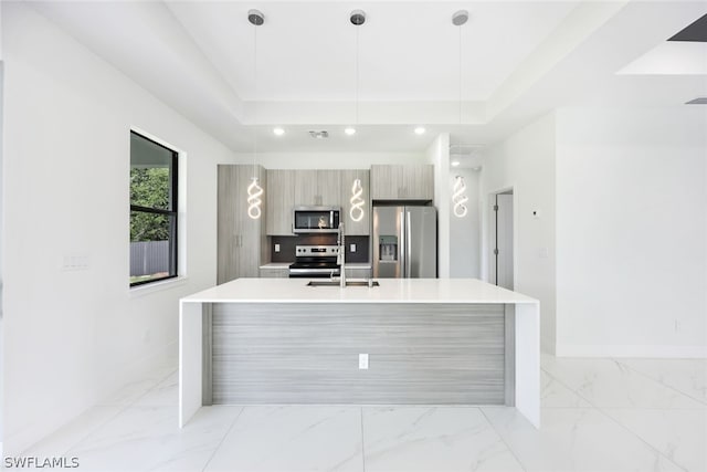 kitchen featuring a tray ceiling, a kitchen island with sink, hanging light fixtures, and stainless steel appliances