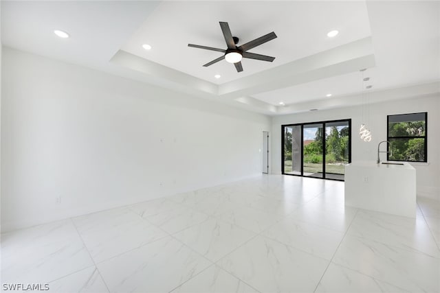 unfurnished room with a raised ceiling, ceiling fan, and sink