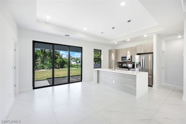 kitchen featuring appliances with stainless steel finishes, a tray ceiling, a kitchen island with sink, sink, and hanging light fixtures