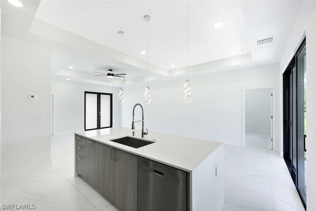 kitchen with a tray ceiling, dishwasher, a center island with sink, and sink