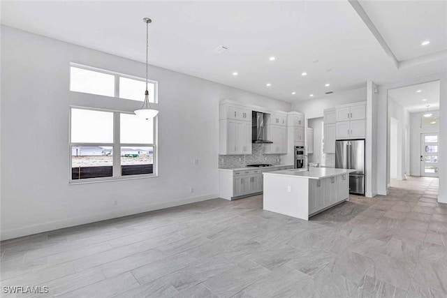 kitchen featuring pendant lighting, stainless steel refrigerator, white cabinets, a kitchen island with sink, and wall chimney range hood