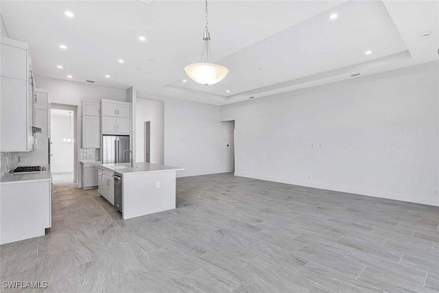 kitchen with white cabinetry, decorative light fixtures, appliances with stainless steel finishes, a tray ceiling, and a kitchen island with sink