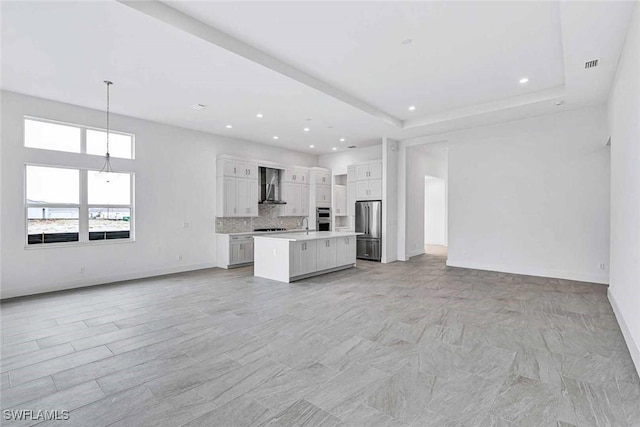 kitchen with pendant lighting, stainless steel appliances, white cabinets, a kitchen island, and wall chimney exhaust hood