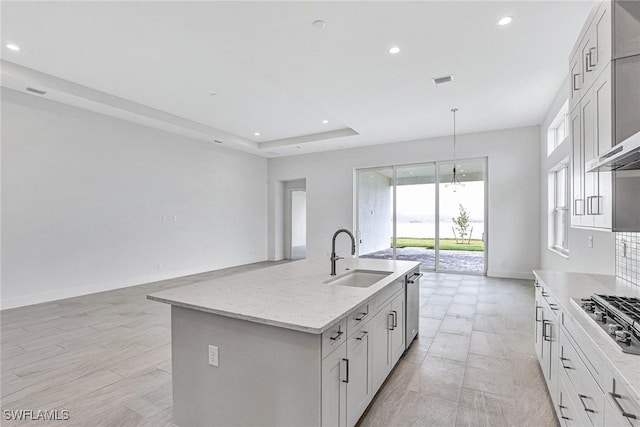 kitchen with sink, white cabinetry, stainless steel appliances, light stone countertops, and a kitchen island with sink