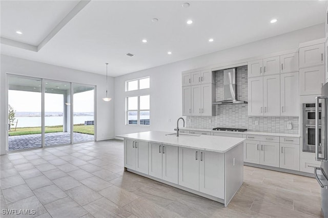 kitchen featuring wall chimney exhaust hood, sink, a water view, stainless steel appliances, and a kitchen island with sink