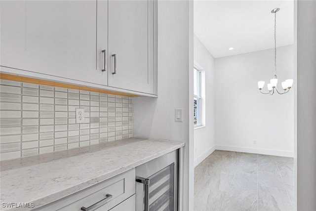 kitchen with an inviting chandelier, wine cooler, light stone counters, tasteful backsplash, and decorative light fixtures