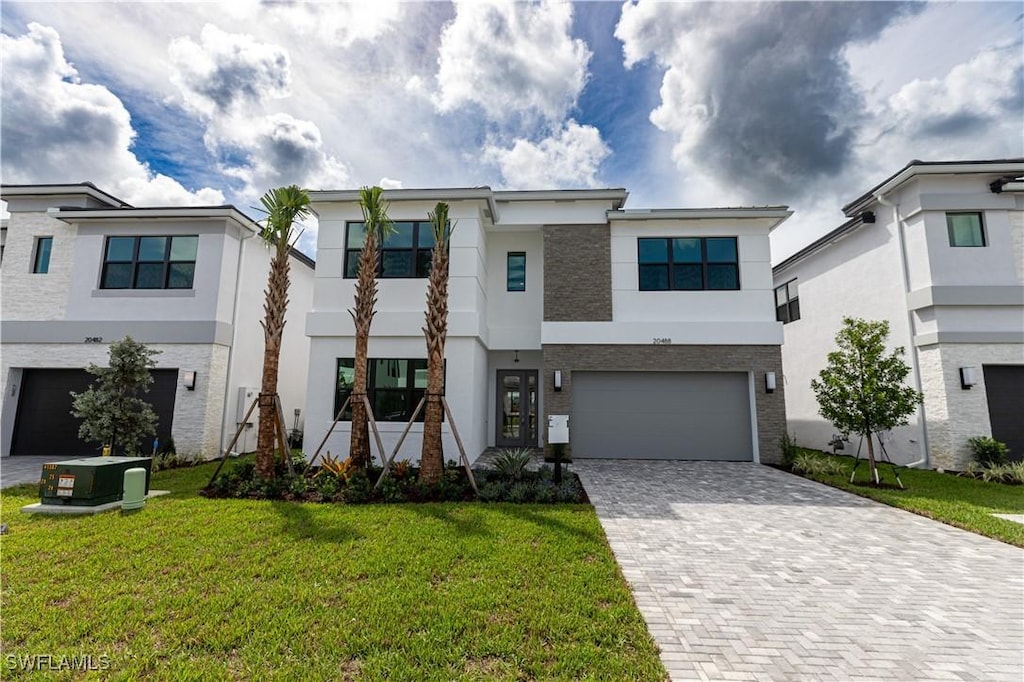 view of front of property featuring decorative driveway, central air condition unit, stucco siding, an attached garage, and a front yard