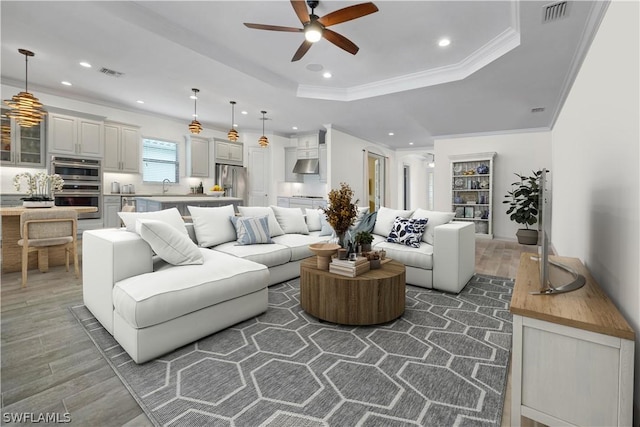 living area featuring visible vents, ornamental molding, a raised ceiling, and wood finished floors