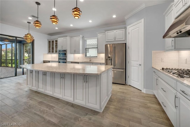 kitchen featuring under cabinet range hood, a sink, a kitchen island, white cabinetry, and appliances with stainless steel finishes