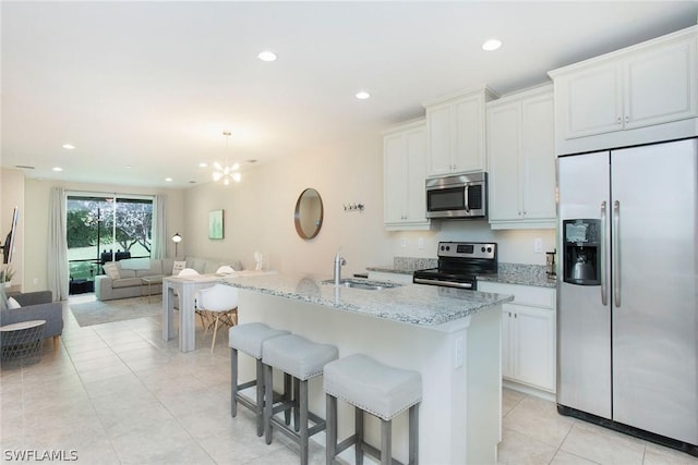 kitchen with light stone counters, white cabinetry, a kitchen island with sink, and appliances with stainless steel finishes