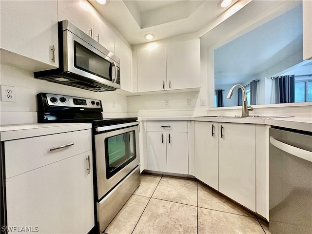 kitchen with light tile patterned floors, stainless steel appliances, light countertops, white cabinetry, and a sink