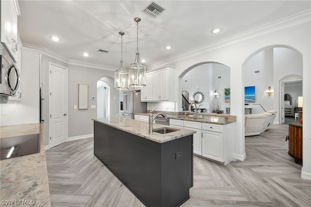 kitchen with pendant lighting, sink, white cabinetry, light stone countertops, and an island with sink