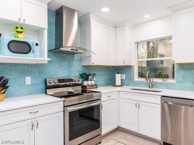 kitchen featuring appliances with stainless steel finishes, white cabinets, wall chimney exhaust hood, backsplash, and sink