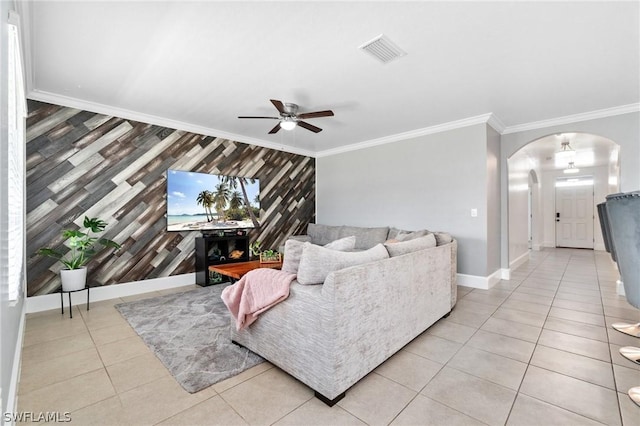 tiled living room with ceiling fan, ornamental molding, and wood walls