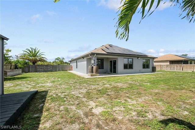 rear view of property featuring a lawn and solar panels