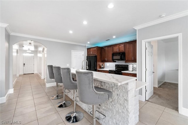 kitchen with backsplash, an island with sink, crown molding, and black appliances