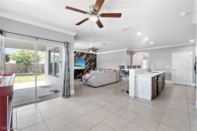 kitchen with ceiling fan, sink, crown molding, a kitchen island with sink, and light tile patterned floors