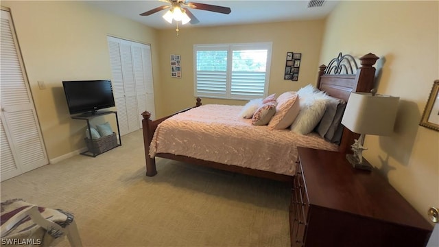 bedroom featuring ceiling fan, light colored carpet, and two closets