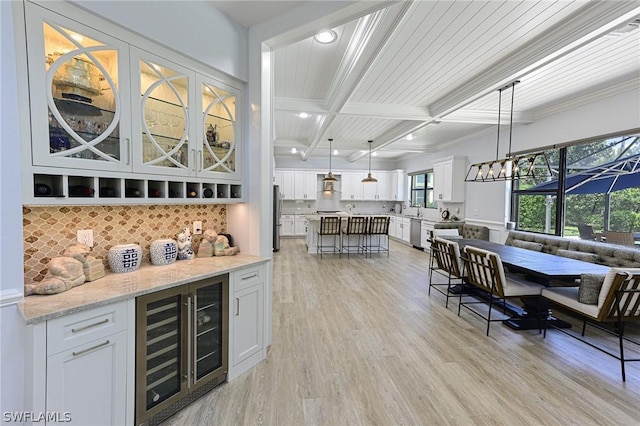 bar with light stone countertops, stainless steel appliances, pendant lighting, white cabinets, and wine cooler