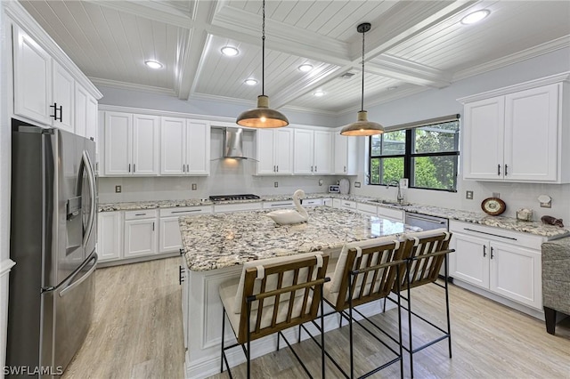 kitchen featuring wall chimney exhaust hood, stainless steel appliances, decorative light fixtures, white cabinets, and an island with sink