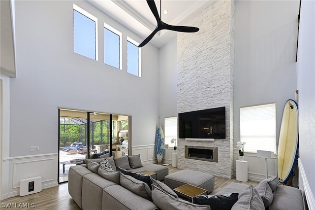 living room featuring a stone fireplace, ceiling fan, a towering ceiling, and light wood-type flooring