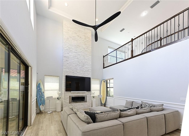 living room with a towering ceiling, ceiling fan, crown molding, a fireplace, and light hardwood / wood-style floors