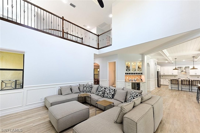 living room with beamed ceiling, a high ceiling, light hardwood / wood-style floors, and beverage cooler