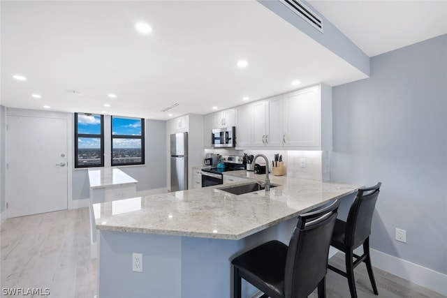 kitchen featuring kitchen peninsula, stainless steel appliances, sink, white cabinets, and light hardwood / wood-style floors