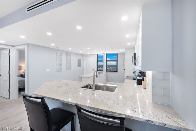 kitchen with kitchen peninsula, light stone counters, white cabinetry, and sink