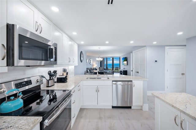 kitchen with an inviting chandelier, kitchen peninsula, light wood-type flooring, appliances with stainless steel finishes, and white cabinetry