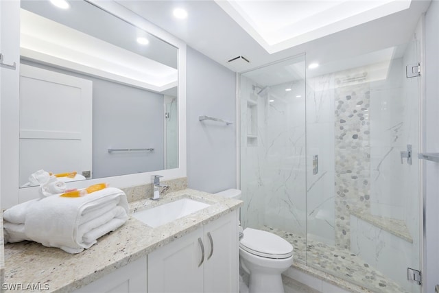 bathroom with a tray ceiling, a shower with door, vanity, and toilet