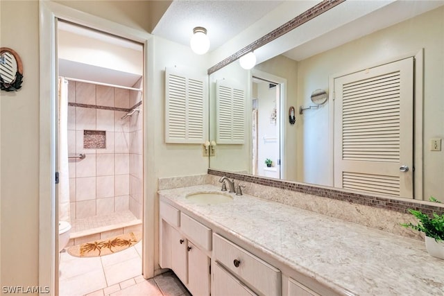 bathroom featuring toilet, tile patterned flooring, tiled shower, and vanity