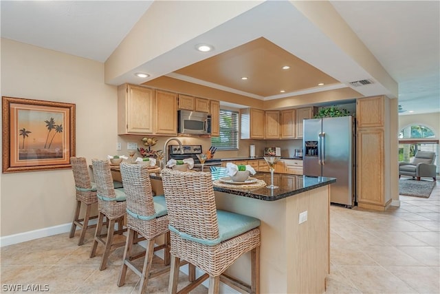 kitchen with kitchen peninsula, light brown cabinetry, stainless steel appliances, and dark stone counters