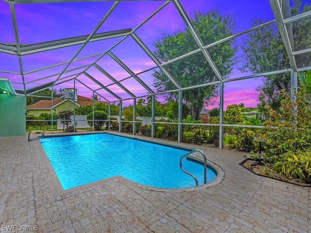 pool at dusk featuring glass enclosure and a patio area